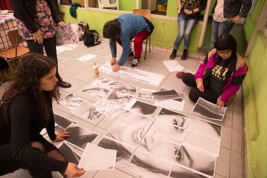 En una sala un grupo de mujeres está organizando y reconstruyendo el rostro de una mujer joven que sonrie con papeles impresos en blanco y negro.