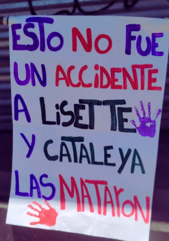 La imagen muestra un cartel con el siguiente mensaje escrito en letras grandes y de diferentes colores: "ESTO NO FUE UN ACCIDENTE A LISETTE Y CATALEYA LAS MATARON" El cartel incluye dos huellas de manos pintadas, una en morado junto a "LISETTE" y otra en rojo junto a "MATARON".